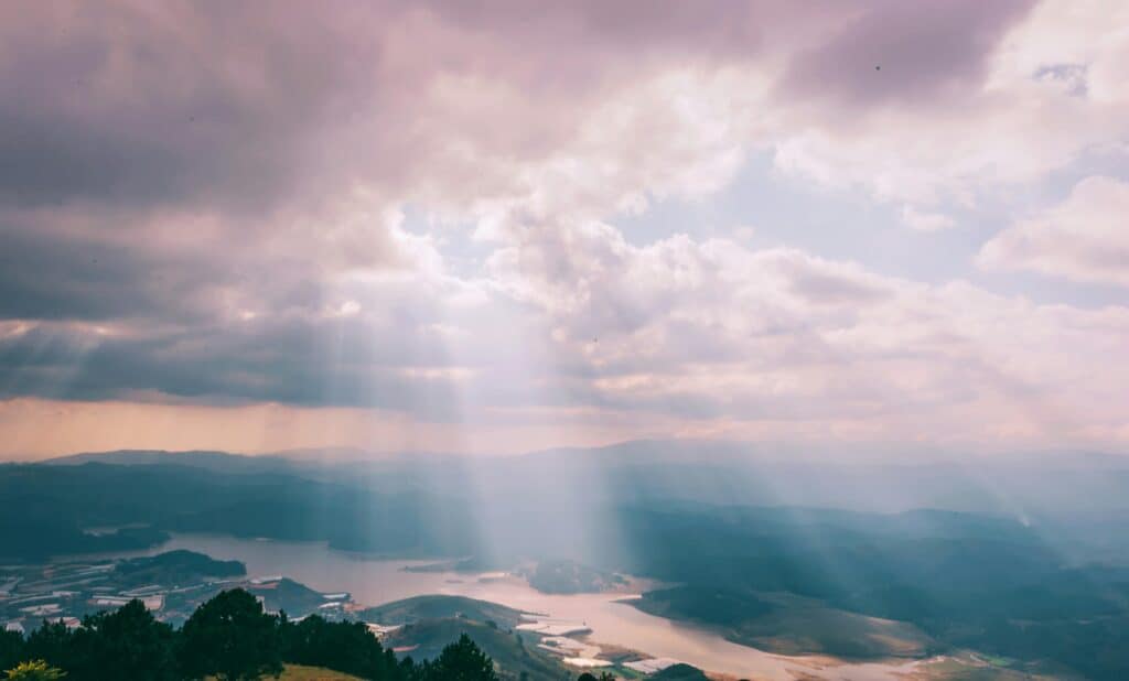 Gentle sunbeams breaking through a cloudy sky over a serene landscape.